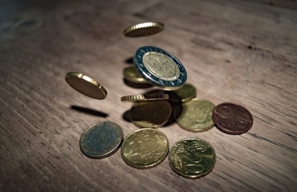 Euro coins, including 1 and 2 euro denominations, scattered on a wooden surface with some coins in mid-air.