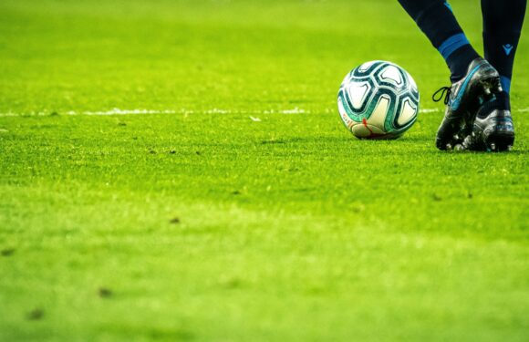 A soccer player in black and blue gear is about to kick a patterned white, green, and red ball on a bright green grass field.