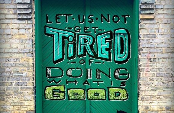 A green door with a motivational graffiti message: "Let us not get tired of doing what is good," referencing Galations 6:9, with a brick wall background.
