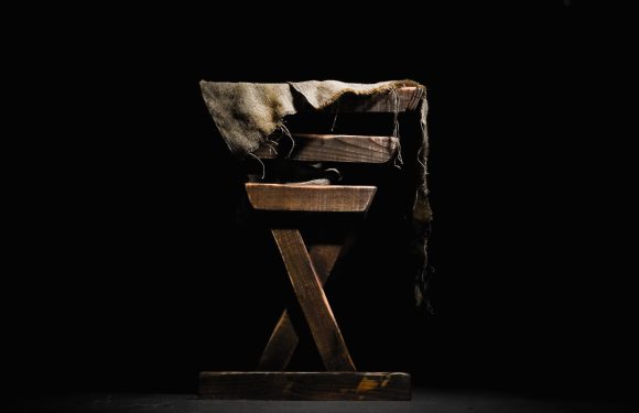 A wooden chair with a torn, faded cloth draped over the top against a black background.