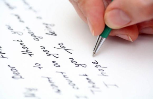 Hand writing a letter with a green pen on white paper.