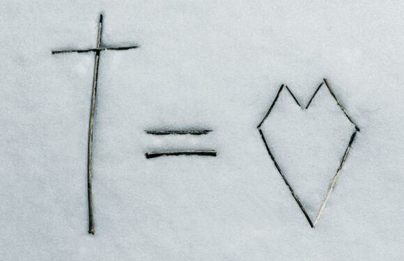 A cross, an equals sign, and a heart shape all made from sticks laid on snow, conveying the message "God equals love."