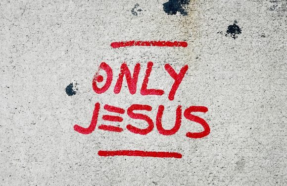 Red graffiti on a white wall that says "ONLY JESUS" with lines above and below the text.