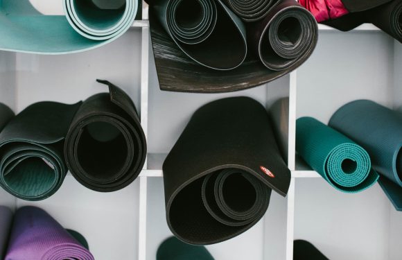 Multiple yoga mats in various colors, including black, purple, teal, and pink, are rolled up and stored on white shelves.