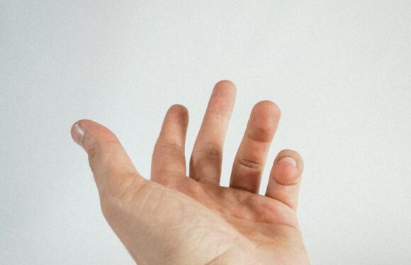 A person's hand reaching out with fingers slightly spread, set against a plain, light-colored background.