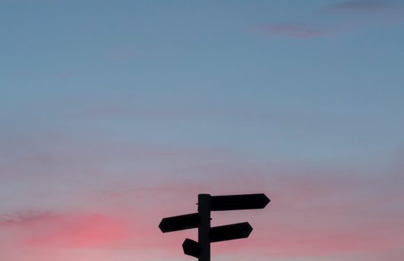 Silhouetted signpost with three directional signs against a colorful sunset sky.