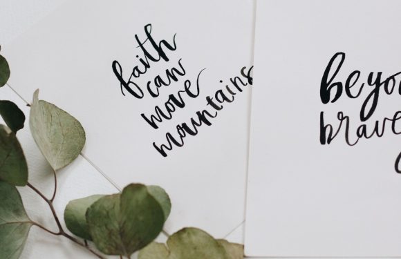 A sprig of dried leaves next to two white cards with black calligraphy, one partially visible, with positive inspirational messages.