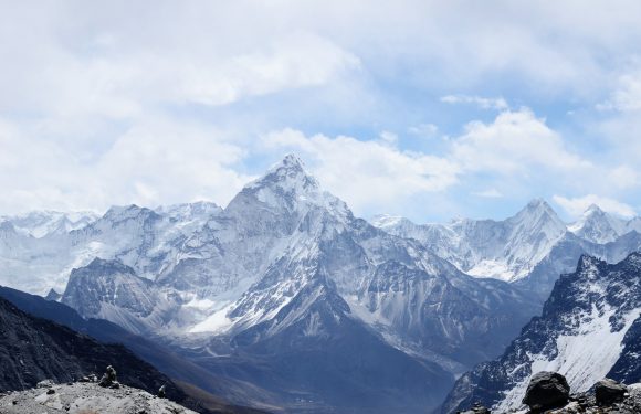 Snow-capped mountains under a partly cloudy sky, with rocky foreground and towering peaks in the distance.