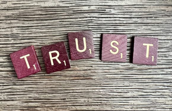 Scrabble tiles spelling "TRUST" on a wooden surface.