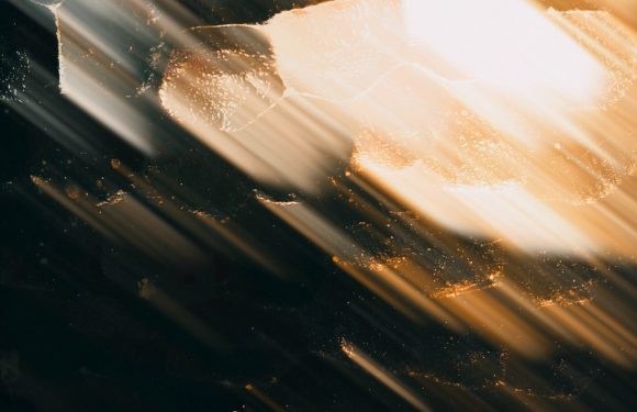 Abstract image with bright streaks of light across dark and golden background, featuring a transparent white shape near the center.