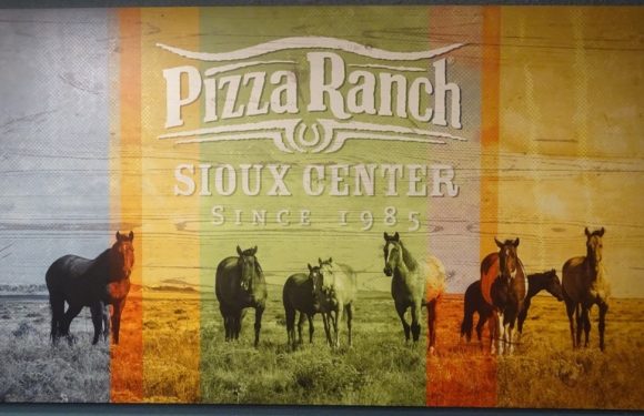 A large sign features seven horses standing in a grassy field, with "Pizza Ranch Sioux Center since 1985" written at the top, designed with a red, yellow, and green motif.