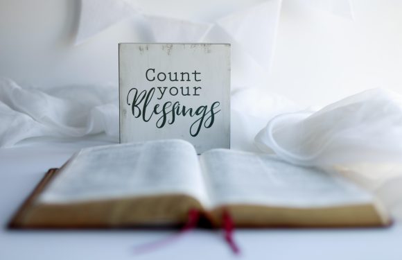 Open Bible with a ribbon bookmark, white fabric, and a sign that reads "Count your blessings."