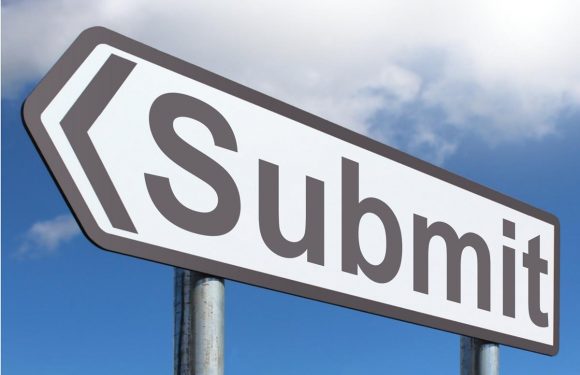 A street sign shaped like the Superman logo with the word "Submit" written on it, set against a partly cloudy sky.