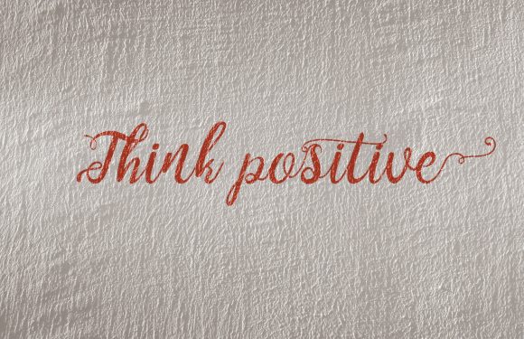 "Think positive" written in a cursive red font on a textured, beige wall background.