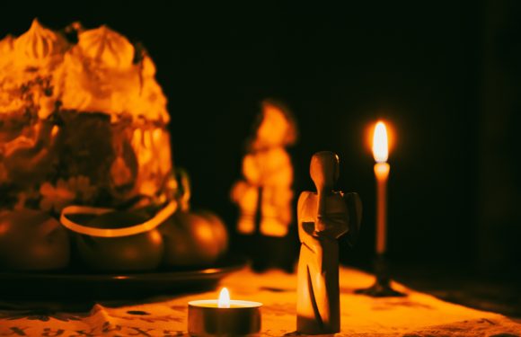 A small figure, candles, and a partially visible cake on a table, with the scene lit by warm candlelight against a dark background.