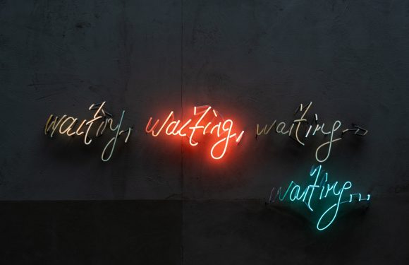 Neon sign on a dark wall says "waiting," repeated three times in different colors, with the middle one illuminated in red.