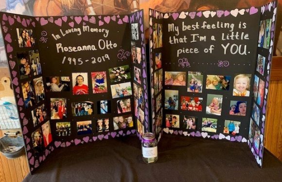 A decorated memorial display board with photos and messages, honoring Roseanna Otto (1995-2019), featuring purple heart-themed borders and candles.