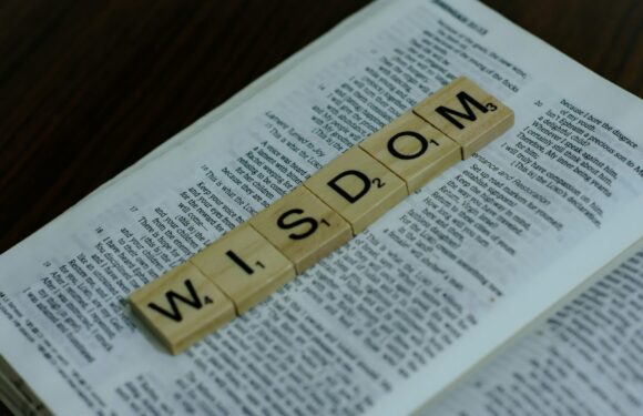 Scrabble tiles spell "WIELD SOME" on an open Bible on a wooden surface.