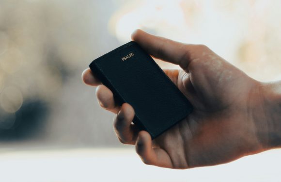 A person holding a black small book or organizer labeled "PSALMS" in their hand, with a blurred, light-colored background.