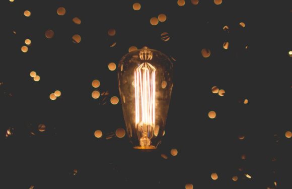A glowing filament light bulb is illuminated amidst blurred golden bokeh lights on a dark background.