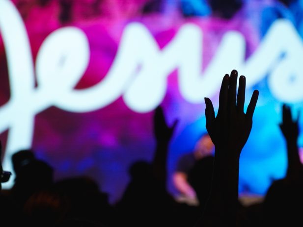 Shadow of hands lifted in praise with the name "Jesus" behind them.