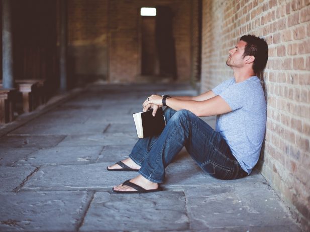 Man sitting on ground with eyes closed and holding Bible.