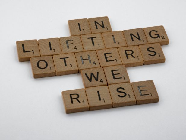Scrabble Letters that say "In Lifting Others We Rise"