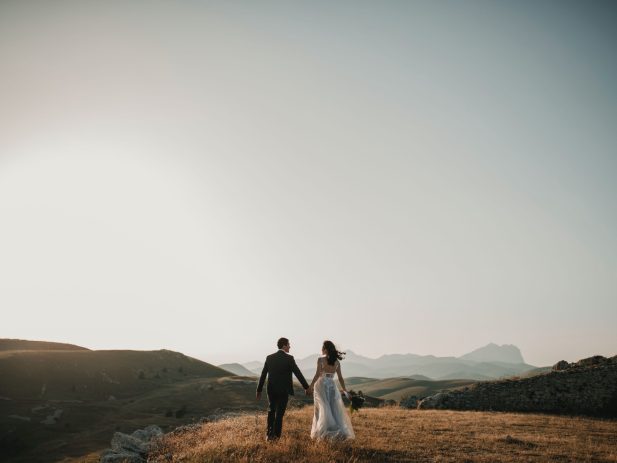 Groom and bride holding hands on hill top.