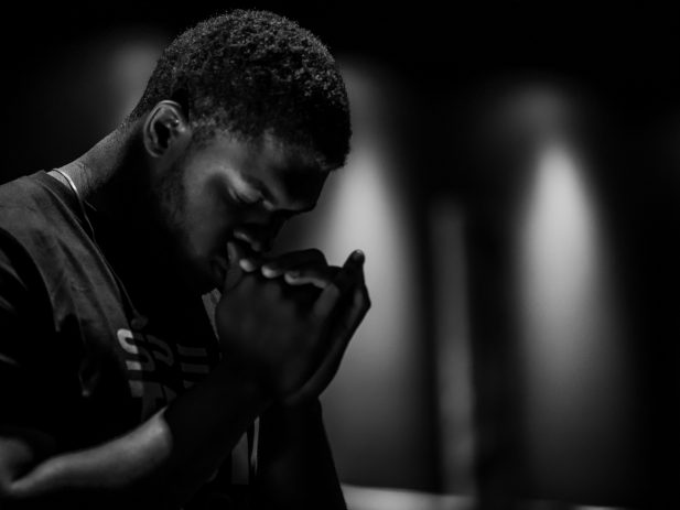 Black and white photo of a man bowing his head and folding his hands to pray