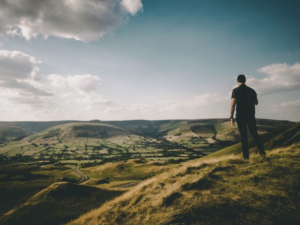 Man standing on hill overlooking green valley.