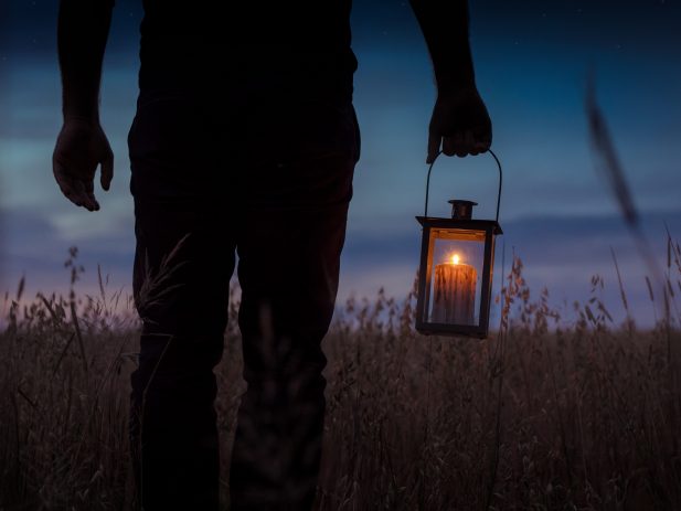 silhouette of person in a grass field at sunset carrying a lantern