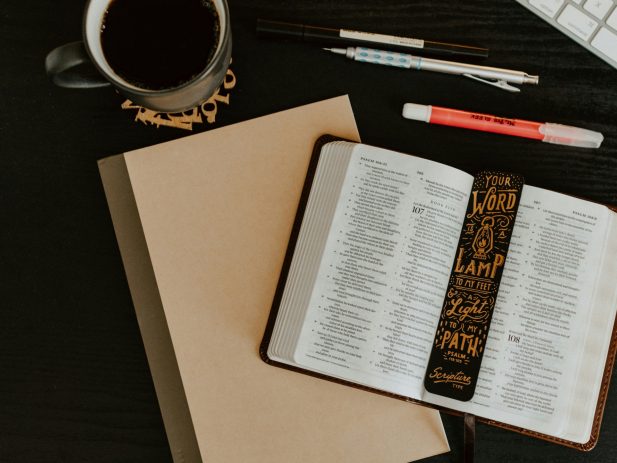 Open Bible on table with coffee and pens.
