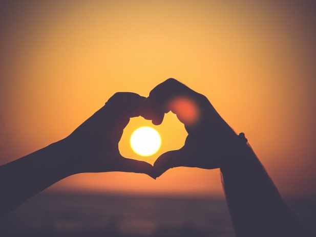 hands in the shape of a heart in front of the sun in a sunset