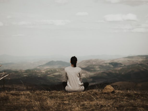 Woman sitting on cliff overlooking mountains.