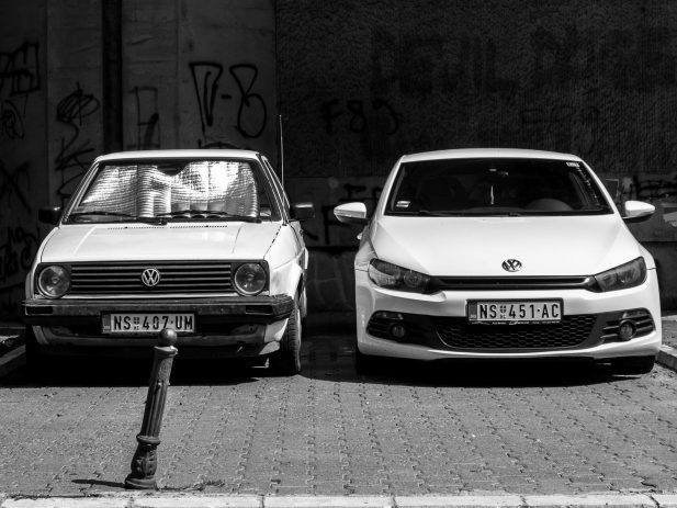 2 Volkswagon cars, both white.  One old and one new.