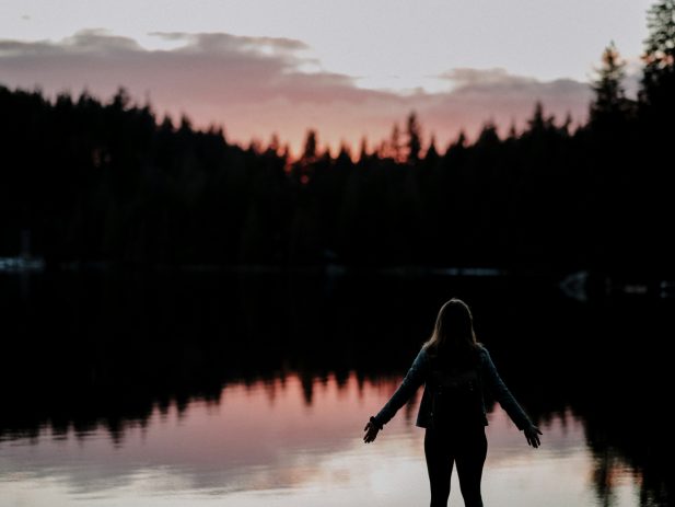 silhouette of a person standing next to a lake at sunset