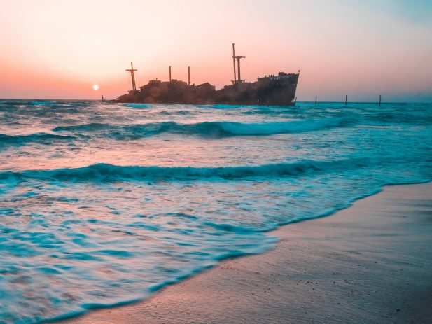 Ocean beach at sunset with wooden ship in background