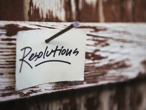 A piece of paper with the word Resolutions written on it nailed to a white painted wood board