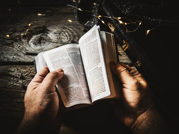 Hands holding open Bible at table.