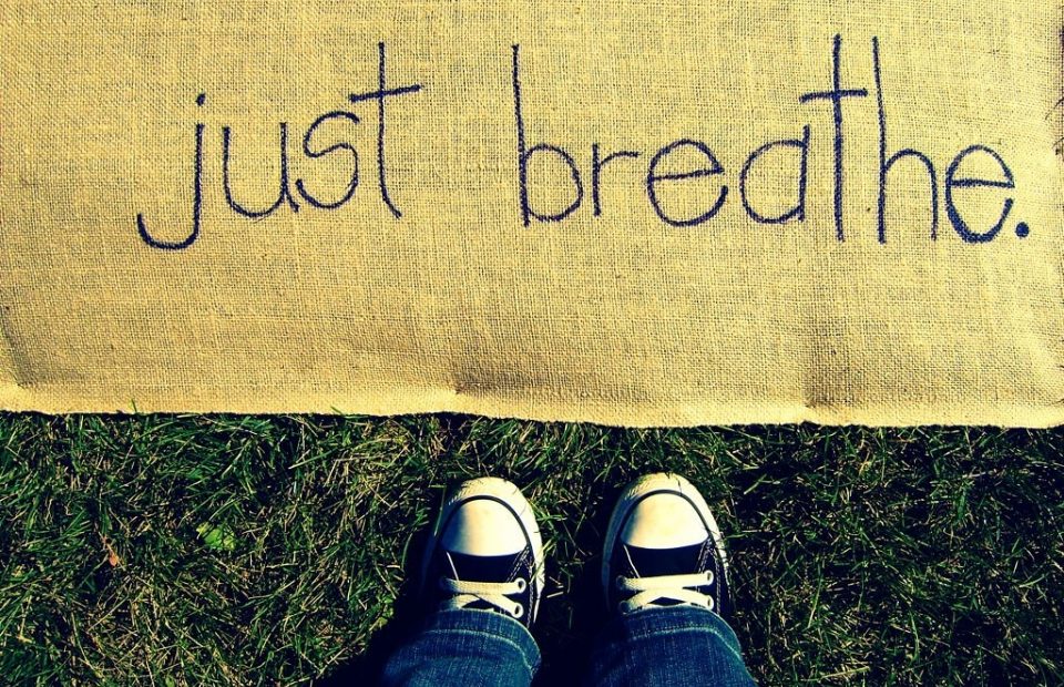 A pair of black and white sneakers worn with jeans, viewed from above, standing on grass next to a yellow mat with the handwritten words "just breathe."