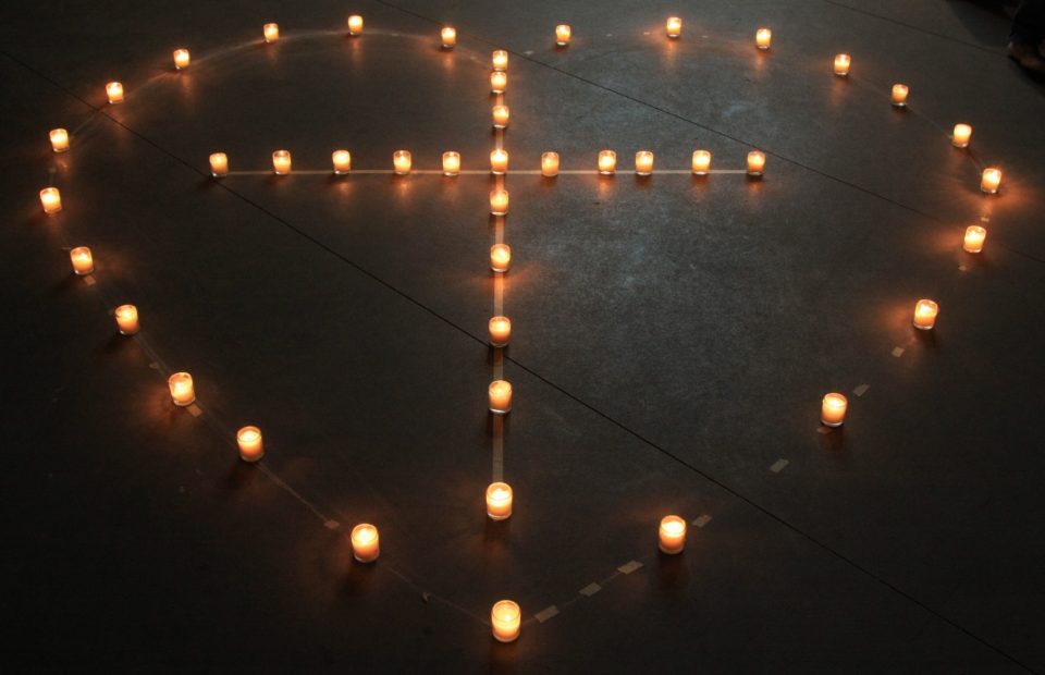 A heart shape created with lit candles on a dark floor, with a peace symbol drawn inside the heart.
