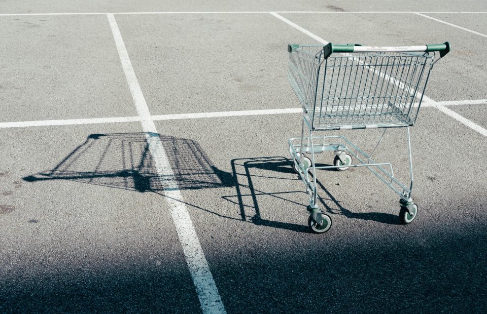 An empty shopping cart casting a shadow on an asphalt parking lot with painted white lines.