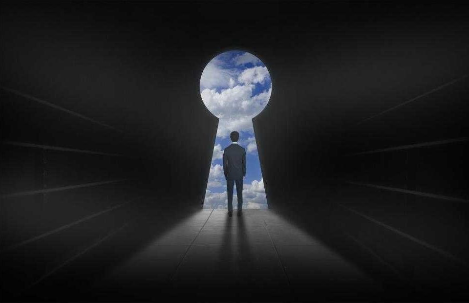 A person in a suit stands in a dark corridor, looking at a keyhole-shaped opening revealing a bright sky with clouds, symbolizing opportunity or discovery.