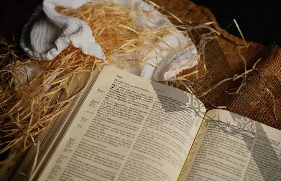 An open Bible resting on straw and burlap fabric, with a white cloth and other textiles nearby.