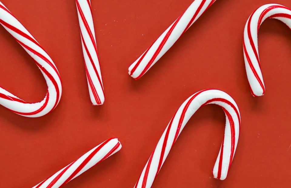 Several red and white striped candy canes scattered on a red surface, some arranged to form a heart shape.