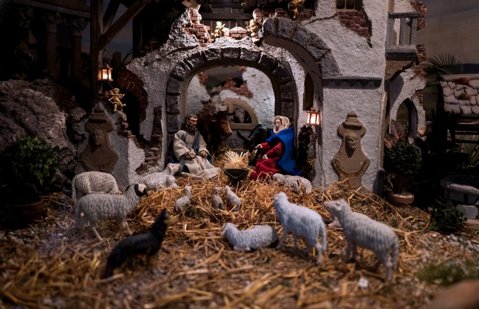 A detailed nativity scene with figurines of Mary, Joseph, baby Jesus, animals, and a stone stable with arches, lanterns, and textured walls.