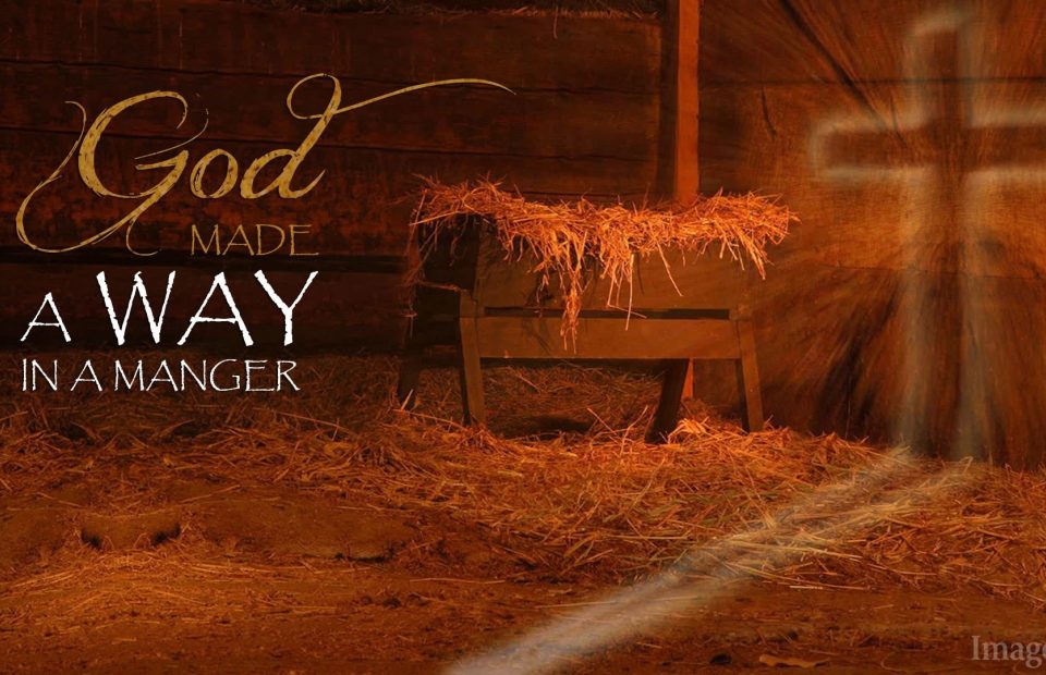 A wooden manger with straw, set against wooden walls, features a religious quote: "God Made a way in a manger," with light rays shining in the background.