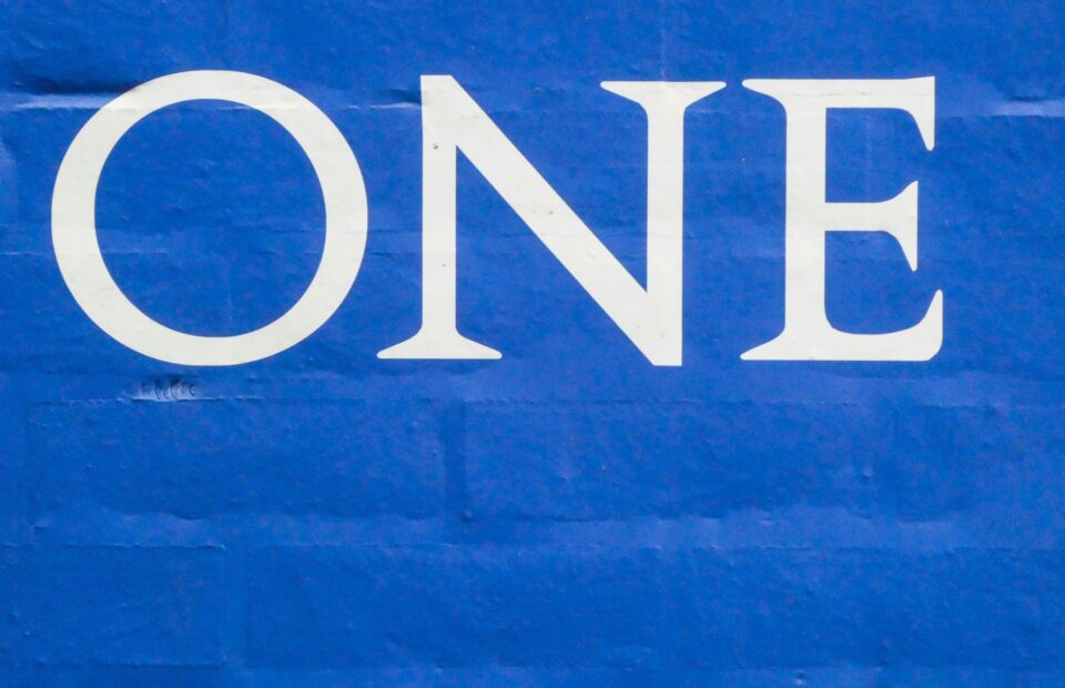 A blue surface with the word "ONE" in large white capital letters. Someone wearing a uniform with a Pizza Ranch logo is visible in the background.