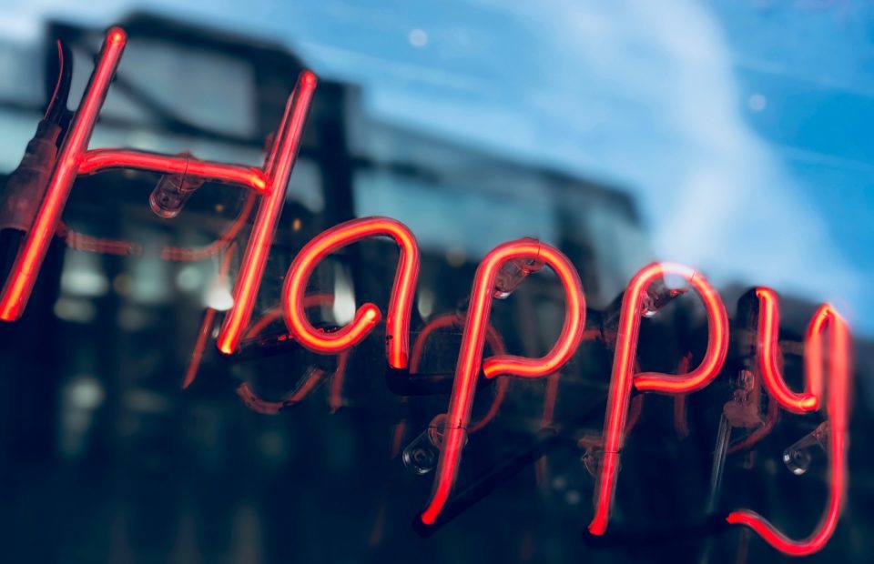 Red neon "Happy" sign with a blue sky reflected in the background.