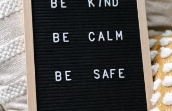 A black felt letter board with white letters displaying the message: "BE KIND, BE CALM, BE SAFE, #SPREAD JOY," leaning against a neutral background.